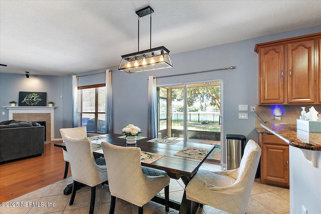 dining area with a textured ceiling, light wood finished floors, and a tile fireplace