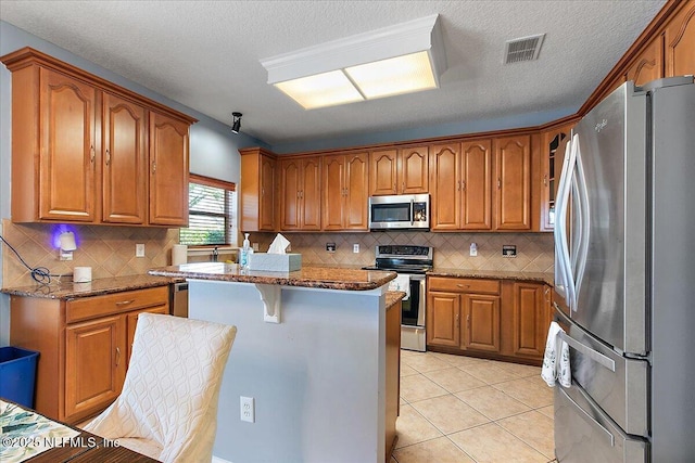 kitchen featuring brown cabinets, a kitchen island, appliances with stainless steel finishes, and light tile patterned flooring