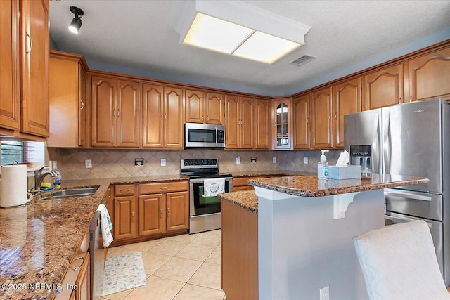 kitchen featuring light tile patterned floors, visible vents, a sink, appliances with stainless steel finishes, and brown cabinets