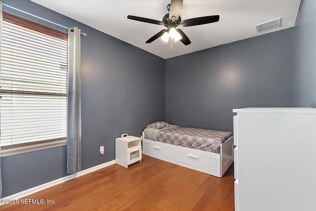 bedroom featuring a ceiling fan, baseboards, wood finished floors, visible vents, and a textured ceiling