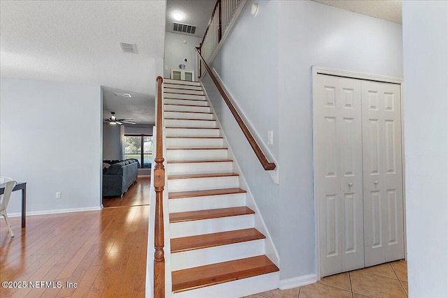 staircase with wood finished floors, baseboards, visible vents, ceiling fan, and a textured ceiling