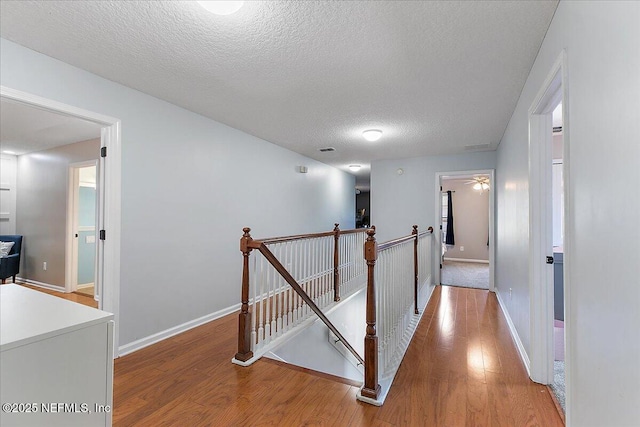 hallway featuring an upstairs landing, a textured ceiling, light wood-type flooring, and baseboards