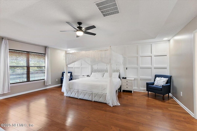 bedroom with visible vents, baseboards, a textured ceiling, and wood finished floors