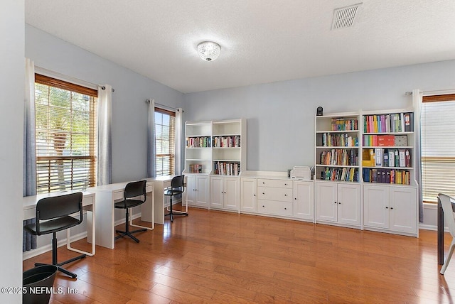 home office with visible vents, baseboards, a textured ceiling, and light wood finished floors