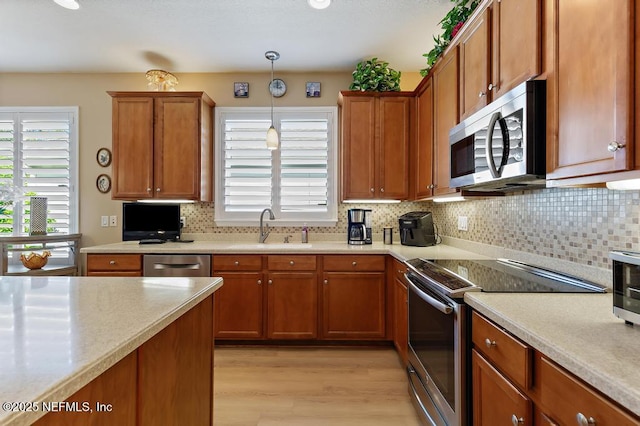 kitchen with a sink, hanging light fixtures, light countertops, appliances with stainless steel finishes, and brown cabinets