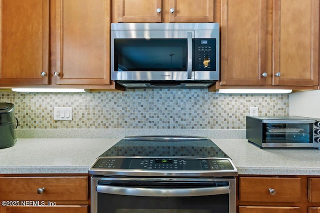 kitchen with a toaster, light countertops, decorative backsplash, brown cabinets, and appliances with stainless steel finishes