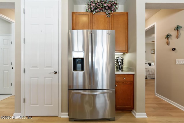 kitchen with baseboards, light countertops, brown cabinets, light wood-style floors, and stainless steel fridge