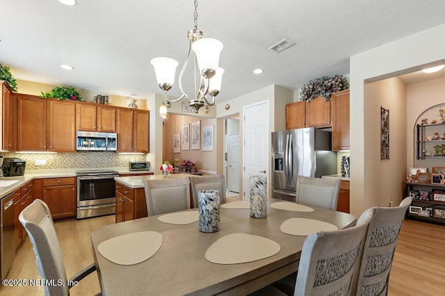 dining space featuring light wood-type flooring, visible vents, a textured ceiling, recessed lighting, and a chandelier