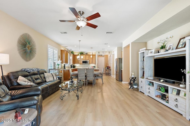 living room with light wood-type flooring, baseboards, visible vents, and ceiling fan