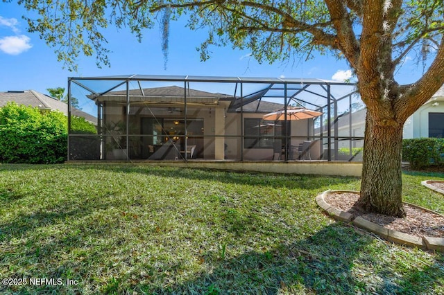 rear view of property with glass enclosure, a yard, and stucco siding