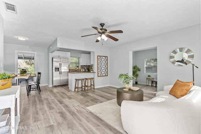 living area featuring light wood-style floors, visible vents, ceiling fan, and baseboards