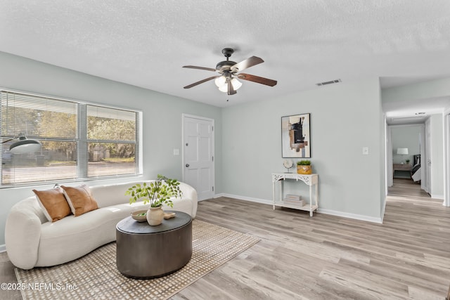 living room with baseboards, a textured ceiling, visible vents, and light wood-style floors