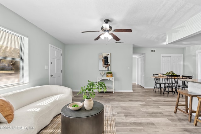 living room featuring light wood-style floors, ceiling fan, visible vents, and baseboards