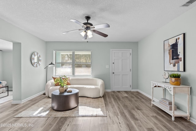 living area with ceiling fan, wood finished floors, visible vents, and baseboards