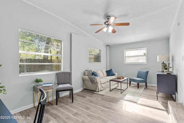 living area with lofted ceiling, ceiling fan, a textured ceiling, baseboards, and light wood-style floors