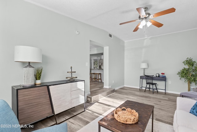 living room featuring a ceiling fan, wood finished floors, visible vents, and baseboards