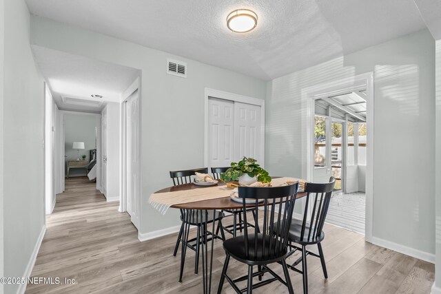 dining space with light wood-style floors, visible vents, a textured ceiling, and baseboards