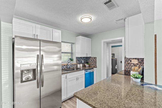 kitchen featuring stainless steel refrigerator with ice dispenser, visible vents, white cabinetry, a sink, and dishwashing machine