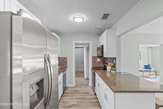 kitchen featuring visible vents, white cabinets, light wood-style flooring, dark stone countertops, and stainless steel appliances