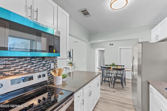 kitchen featuring stainless steel appliances, visible vents, light wood-style floors, white cabinets, and dark stone countertops