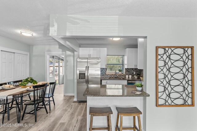 kitchen featuring a breakfast bar, a sink, white cabinetry, light wood finished floors, and stainless steel fridge