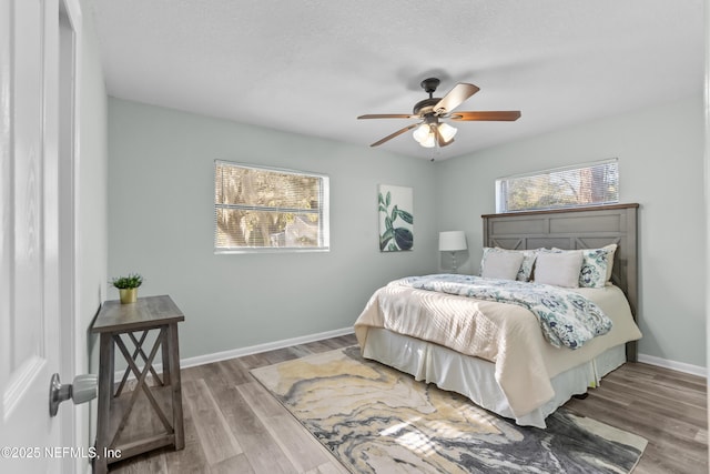 bedroom with multiple windows, ceiling fan, baseboards, and wood finished floors