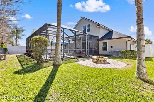 back of house with an outdoor fire pit, a lawn, a patio, a lanai, and fence