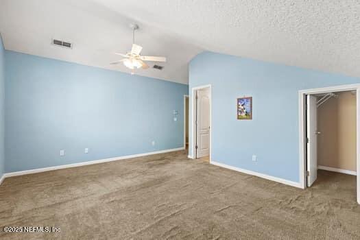 unfurnished bedroom featuring vaulted ceiling, a textured ceiling, carpet, and visible vents