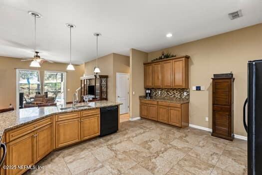 kitchen featuring brown cabinetry, light stone countertops, black appliances, pendant lighting, and a sink