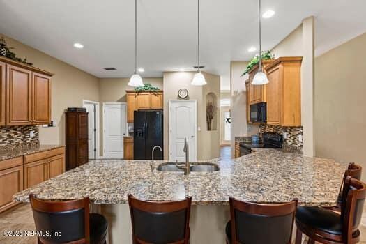 kitchen with a peninsula, black appliances, decorative backsplash, and a sink