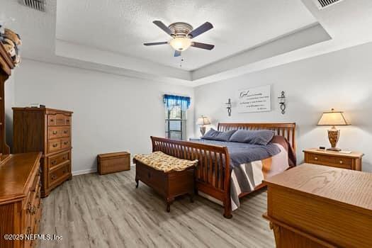 bedroom with a ceiling fan, a tray ceiling, visible vents, and light wood-style flooring