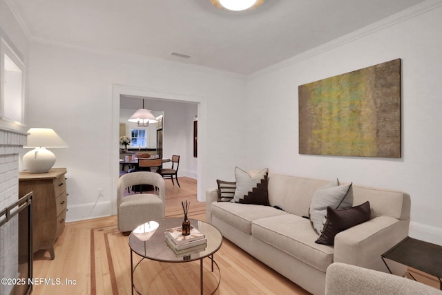 living room with crown molding, visible vents, light wood-style floors, a brick fireplace, and baseboards