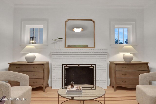 living area with a brick fireplace, light wood-type flooring, and crown molding