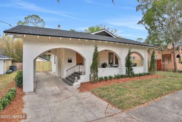 view of front of house with a shingled roof, fence, concrete driveway, and brick siding