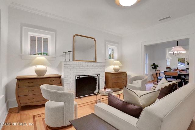 living area featuring a brick fireplace, visible vents, ornamental molding, an inviting chandelier, and light wood-style floors