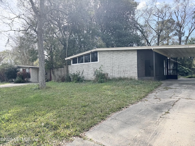 view of side of home featuring an attached carport, concrete block siding, a yard, and driveway