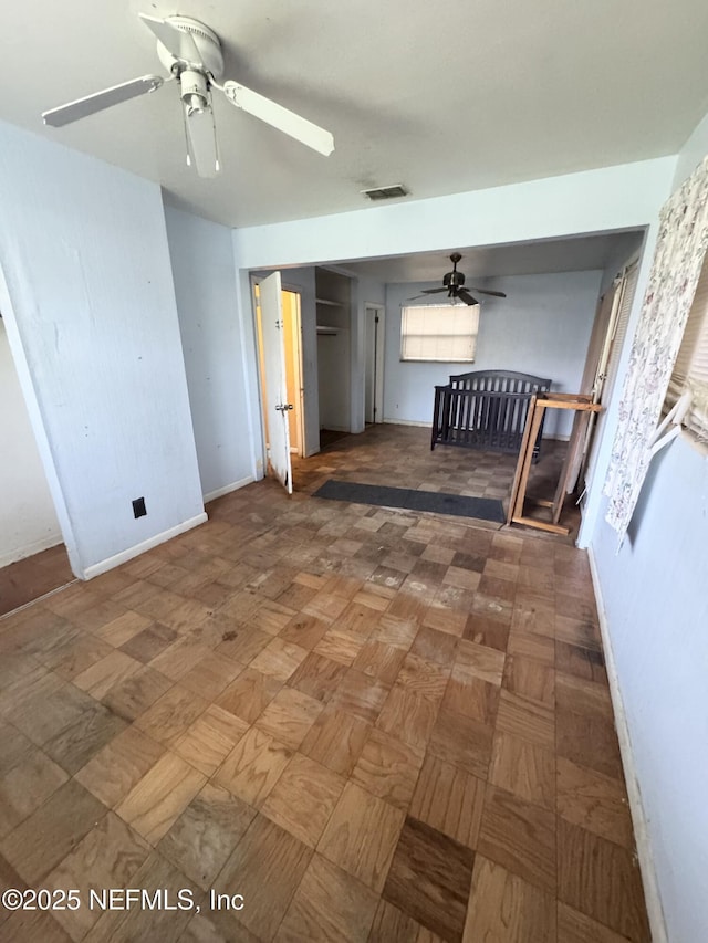 unfurnished living room featuring ceiling fan, visible vents, and baseboards