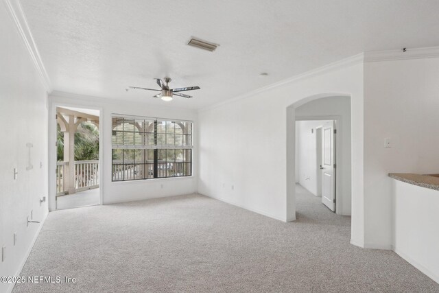 carpeted spare room featuring visible vents, ceiling fan, ornamental molding, arched walkways, and a textured ceiling