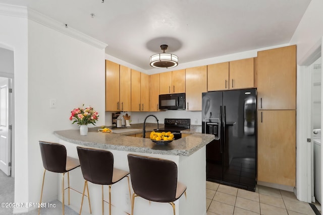 kitchen with light tile patterned floors, a peninsula, black appliances, and a kitchen bar