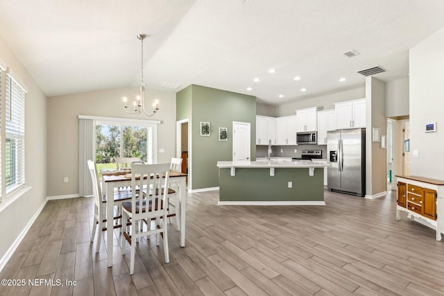 dining area with light wood-style floors, vaulted ceiling, a healthy amount of sunlight, and a notable chandelier