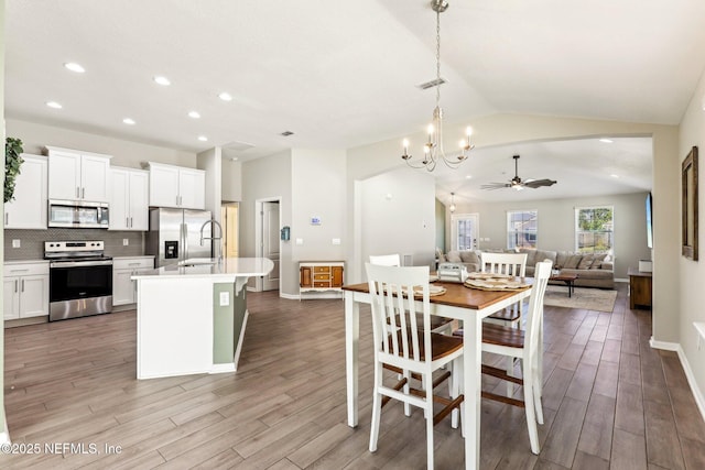 dining room featuring ceiling fan with notable chandelier, visible vents, baseboards, vaulted ceiling, and light wood-type flooring