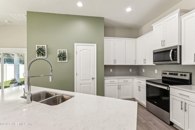 kitchen with light wood-style flooring, stainless steel appliances, a sink, white cabinetry, and decorative backsplash