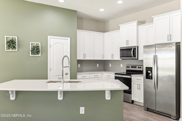 kitchen featuring appliances with stainless steel finishes, white cabinets, a sink, and a breakfast bar area