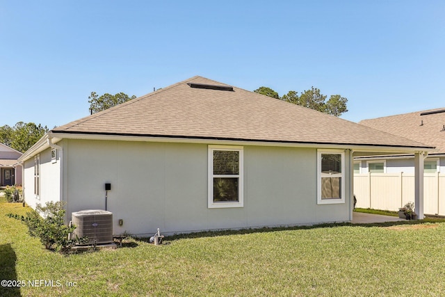 rear view of house with roof with shingles, fence, central AC, and a yard