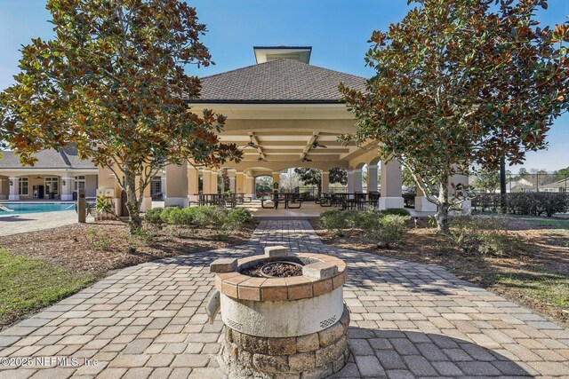 view of patio featuring ceiling fan, a fire pit, and an outdoor pool