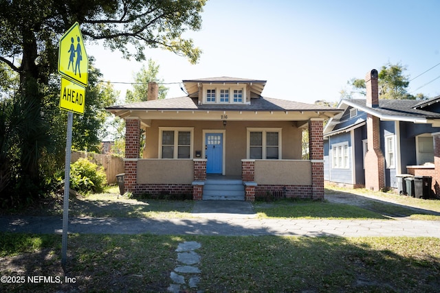 bungalow-style house featuring covered porch, brick siding, and stucco siding