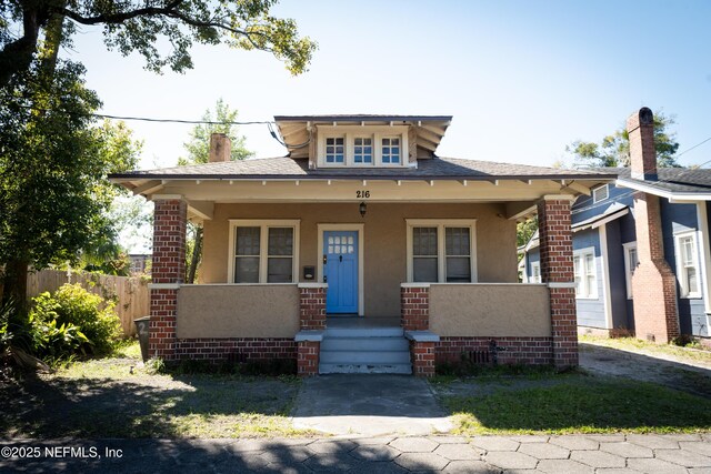 bungalow-style home featuring covered porch, a shingled roof, fence, and stucco siding