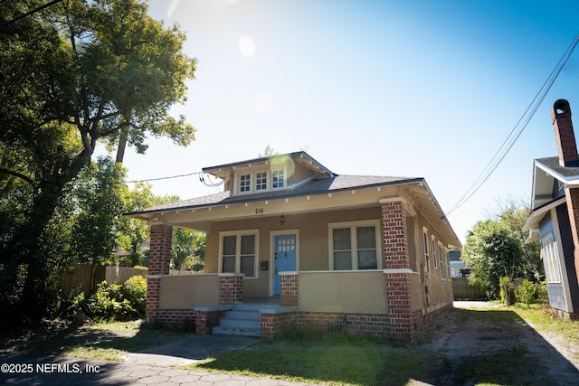 bungalow-style house featuring a porch, fence, brick siding, and stucco siding