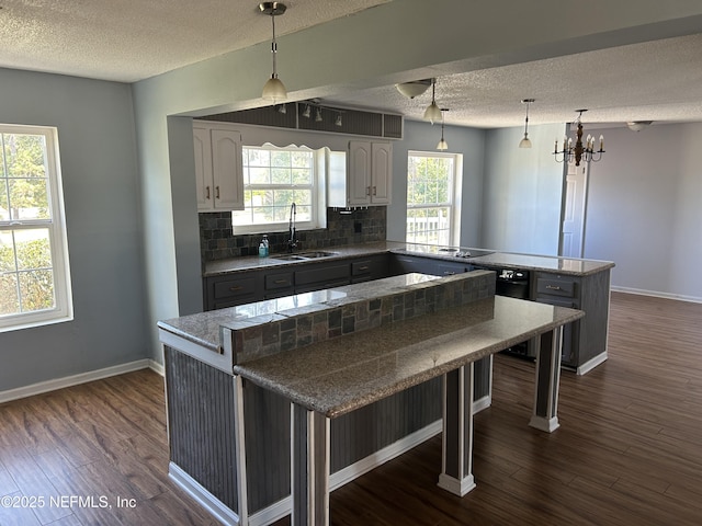 kitchen featuring dark wood finished floors, a peninsula, decorative backsplash, and a sink