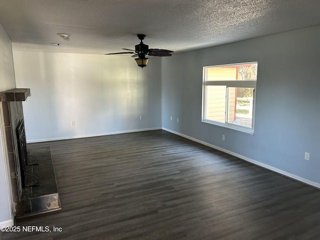 unfurnished living room with a fireplace with raised hearth, a textured ceiling, dark wood-style floors, baseboards, and ceiling fan